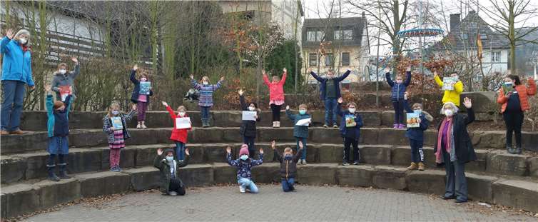 Stellvertretend für ihre Mitschüler*innen halten einige Erst- und Zweitklässler*innen einige der gekauften Bücher in die Kamera. Mit den Schülerinnen freuen sich Anne Mertens vom Schulbüchereiteam (rechts) und die Rektorin Anjo Närdemann.Foto: privat