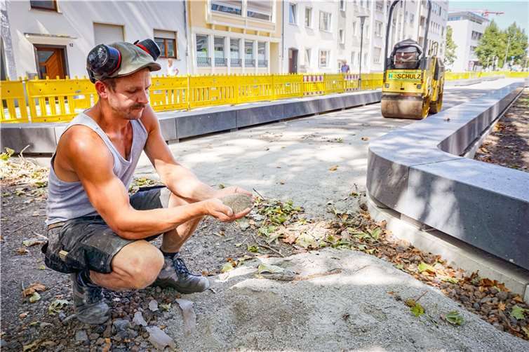 Straßenbauer Nico Klammer zeigt das sandige Material, aus dem die wassergebundene Wegedecke in der Mittelpromenade der Südallee hergestellt wird. Der Weg bleibt wasser- und luftdurchlässig. Foto: Stadt Koblenz / Verena Groß