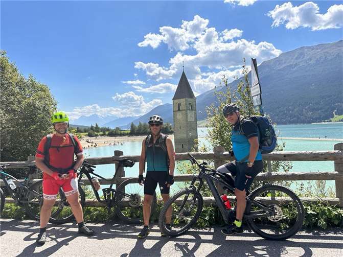 Sven Dau, Gerd Scholze und Andreas Kretschmer vor dem Reschensee. Im Hintergrund der Kirchturm von Alt-Graun: Der im See stehende Kirchturm des untergegangenen Dorfes Graun ist das markanteste Wahrzeichen des Reschensees. Er blieb trotz der Überflutung des Dorfes Graun und des Mittersees durch die Stauung des Reschensees erhalten. Foto: privat