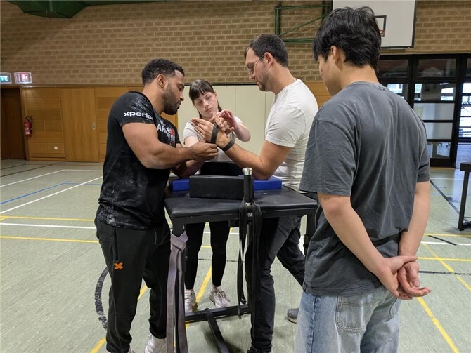 Time Johnson (l.) und Marc Schlendzielorz (r.) bei der Vorbereitung eines Kampfes. Tamara Fastner legt die Strapper an, die verhindern, dass die Hände der Gegner abrutschen, während Long Vu Ninh das Ganze beobachtet.