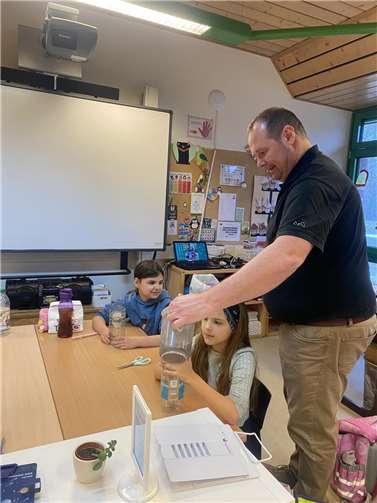 Umweltpädagoge Herr Marc Decker hilft den Kindern der dritten Klasse bei einem Experiment zum Thema "Wasser - ein wertvolles Gut".