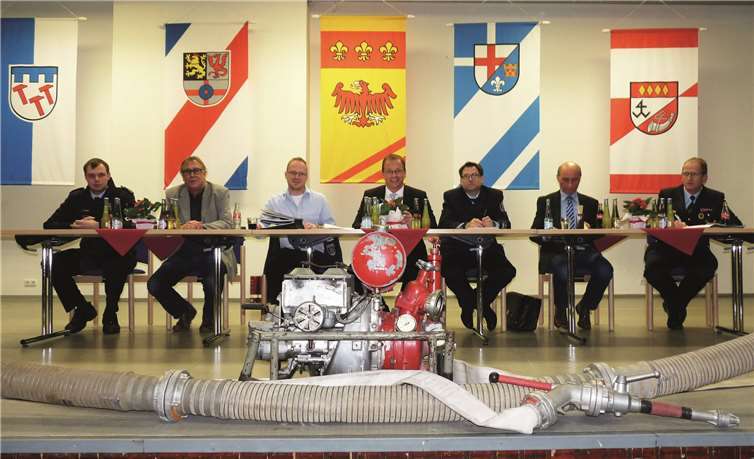 VG-Bürgermeister Jörg Lempertz (Mitte) leitete in seiner Eigenschaft als oberster Chef der VG-Wehren die Veranstaltung. Die FFw Thür hatte die Bühne in der Mehrzweckhalle u.a. mit einer Pumpe aus dem Jahre 1956 dekoriert.