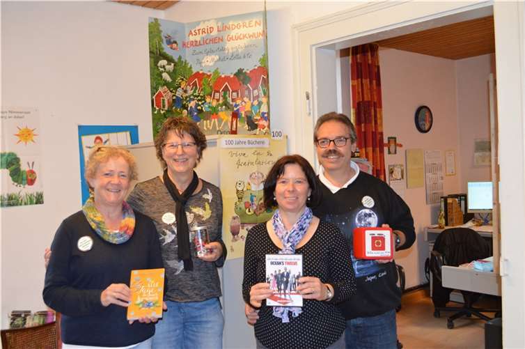 Vier der elf Büchereimitarbeiter unter dem Jubiläumsplakat.