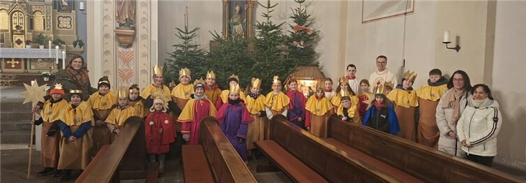 V.l.: Die Sternsingerverantwortlichen Simone Nonn, Ministranten, Pastor Norbert Missong und Daniela Spiller sowie Chridi Samar mit einigen Sternsingern bei den drei Königen an der Krippe. Foto: Andreas Ommer