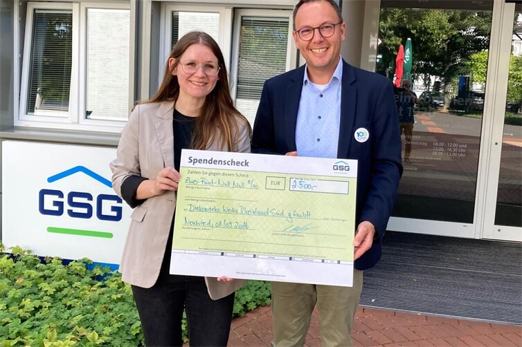 Vor dem Eingang der kommunalen Wohnungsgesellschaft überreichte GSG-Geschäftsführer David Meurer einen symbolischen Scheck an Sarah Fischer, die bei der Diakonie für Allgemeine Sozialberatung und Migrationsberatung zuständig ist.