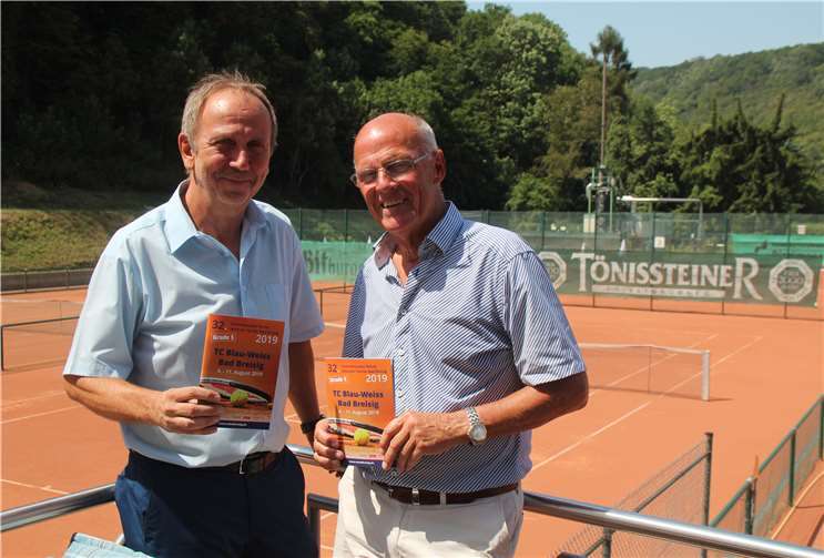 Vor der Tennisanlage des TC Blau Weiß präsentieren Vereinsvorsitzender Walter Erben und Turnierdirektor Uli Adams (v.r.) die druckfrische Broschüre zum 32. Internationalen Senioren-Tennisturnier, die auch über das Rahmenprogramm informiert.