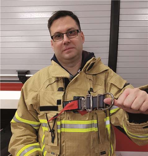 Wehrleiter Stephan Schüller weist auf eine innenliegende Rettungsschlaufe an seinem neuen Schutzanzug hin.