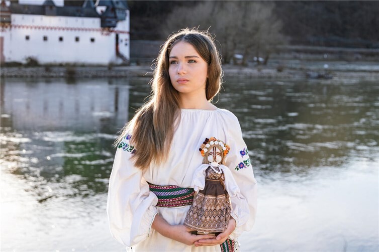 Wyschywanka am Rhein: Eine Frau in ukrainischer Tracht hält eine Motanka-Puppe in den Händen — zwei Kulturen, ein Bild.