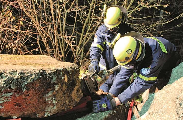 Zwei THW-Helfer heben einen Steinbrocken mit der hydraulischen Schere an.