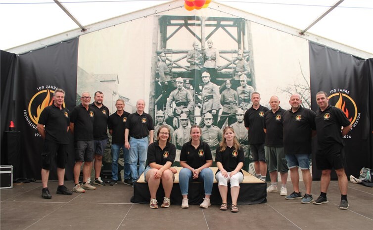 Zwölf Mitglieder der Freiwilligen Feuerwehr Westum beim Jubiläumsfest, darunter Löschgruppenführer Tobias Michels (2. von rechts) sowie einige „Vorgänger“ (historischen Bild im Hintergrund).  Fotos: DU