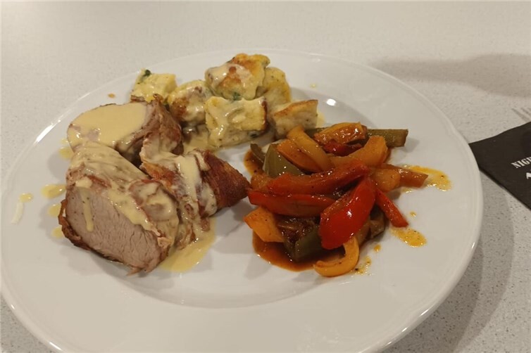 die Hauptspeise Schweinefilet im Speckmantel, Kräuter-Gnocchi, Paprikagemüse